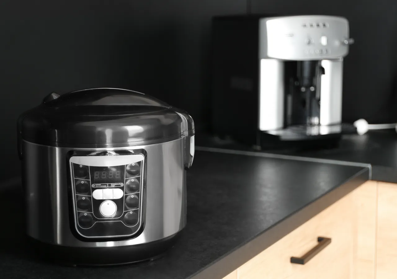 A multicooker and a coffee machine sitting side by side on a dark kitchen benchtop.