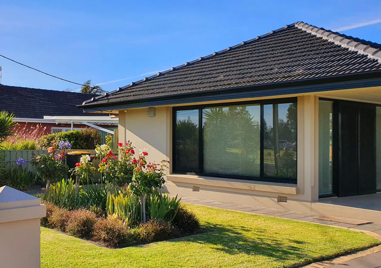 A single-storey brick veneer home behind a flowering front garden.