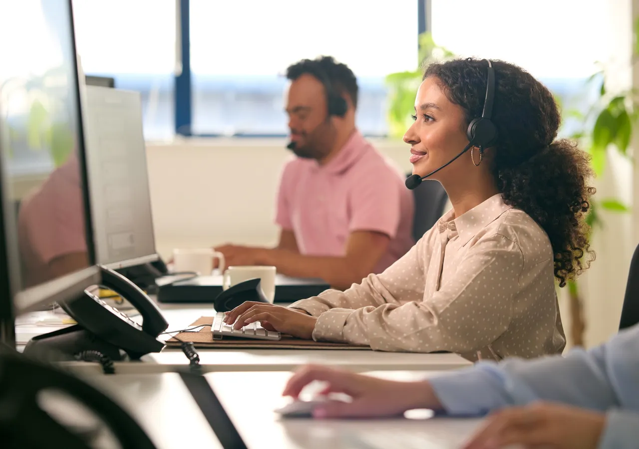 Two energy company staff working at computers in an open-plan office, one wearing a headset.