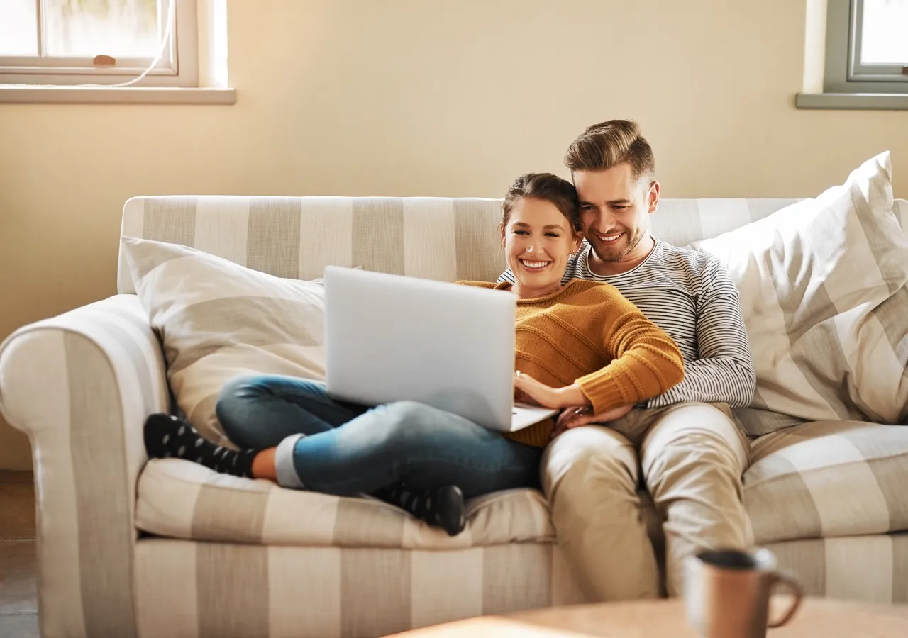 A couple sitting together on a sofa looking at a laptop screen.