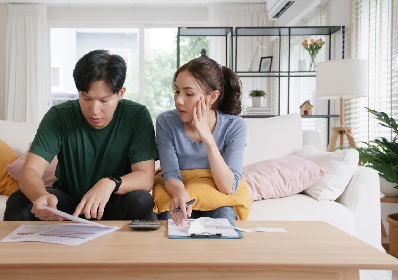 Two people sitting on a sofa going through printed statements together, one holding a pen.