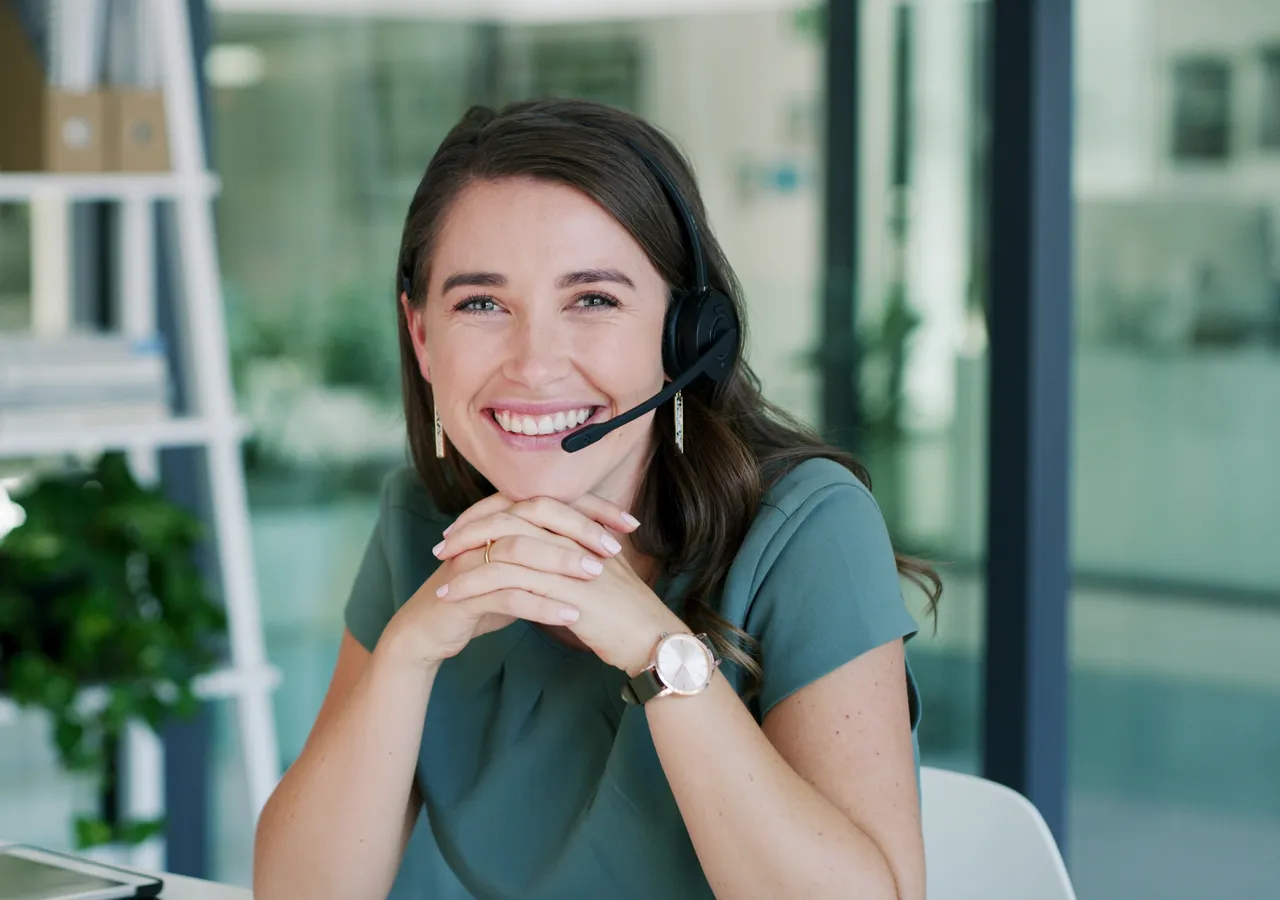 A customer service representative wearing a headset, seated at an office desk.