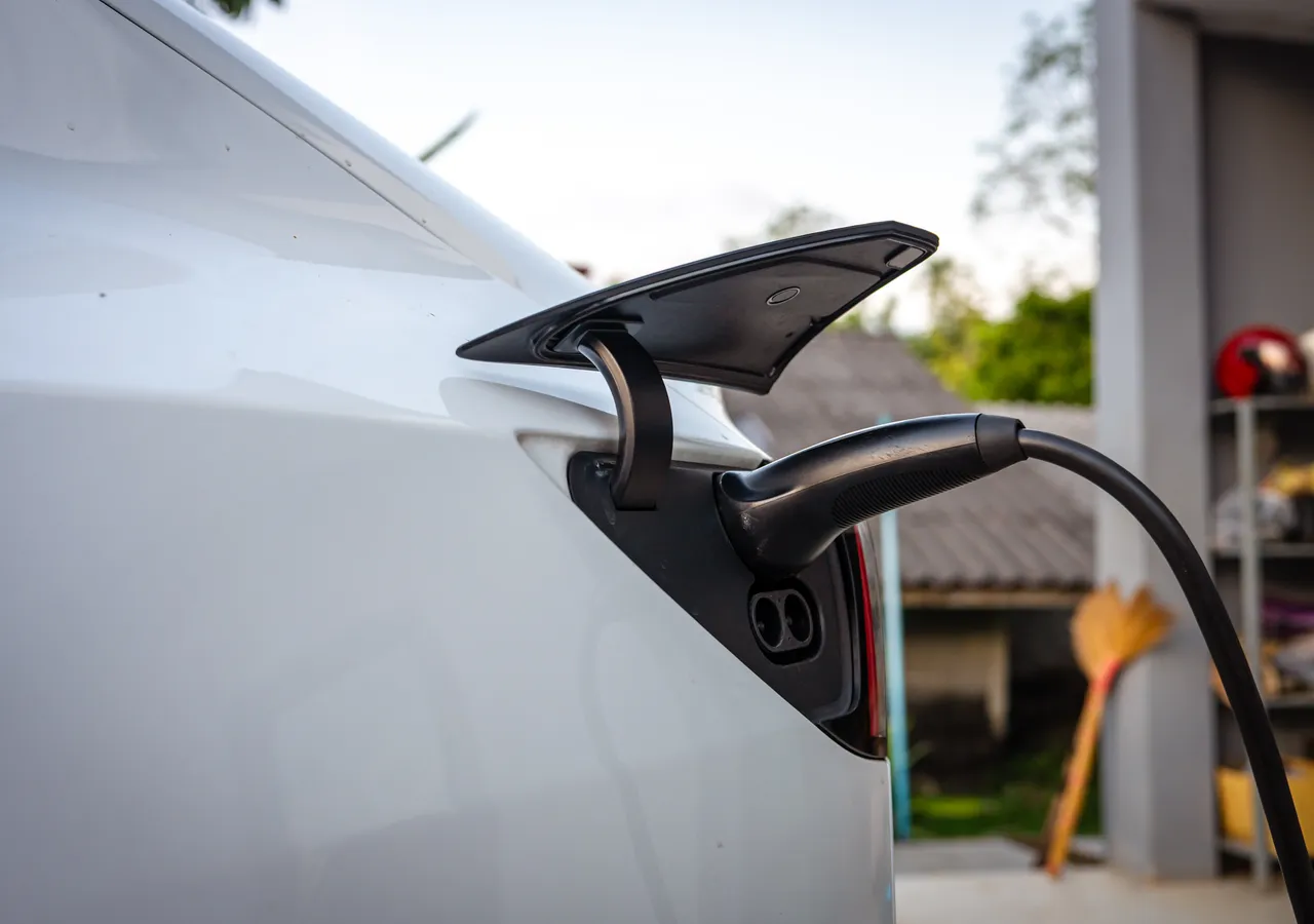 A charging cable plugged into the charge port of a white electric car parked inside a domestic garage.