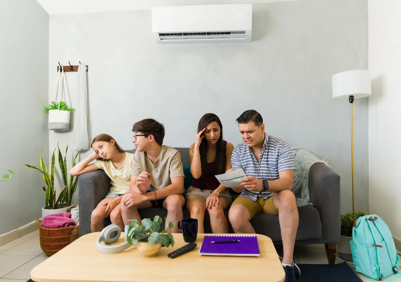 A family sitting together on a lounge suite with a wall-mounted split system air conditioner above them.