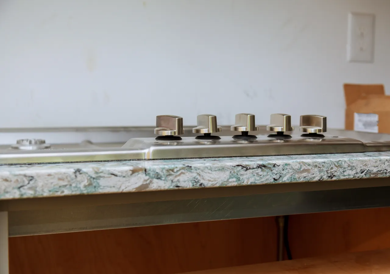 A gas cooktop set into a wide stone kitchen benchtop, unused, with the burner controls in a row along the front edge.
