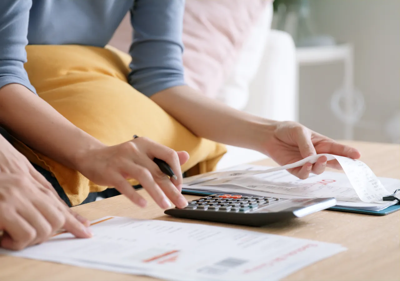 Close view of two people working through printed statements on a table, one using a calculator.