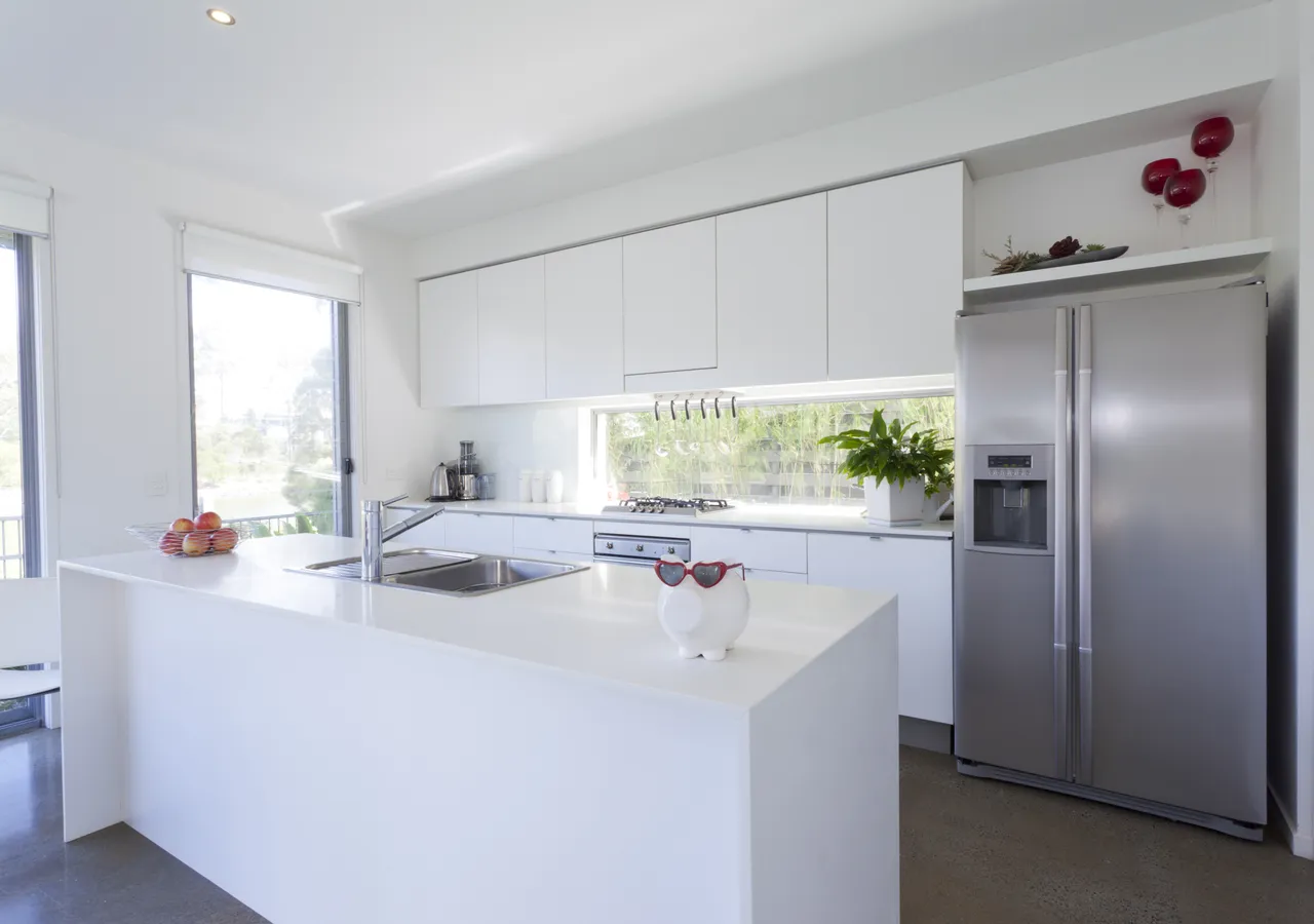 A bright white modern kitchen with a large stainless steel refrigerator against the far wall.