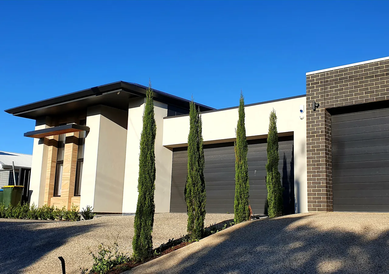 A row of modern rendered townhouses with roller-door garages and clipped conifers.