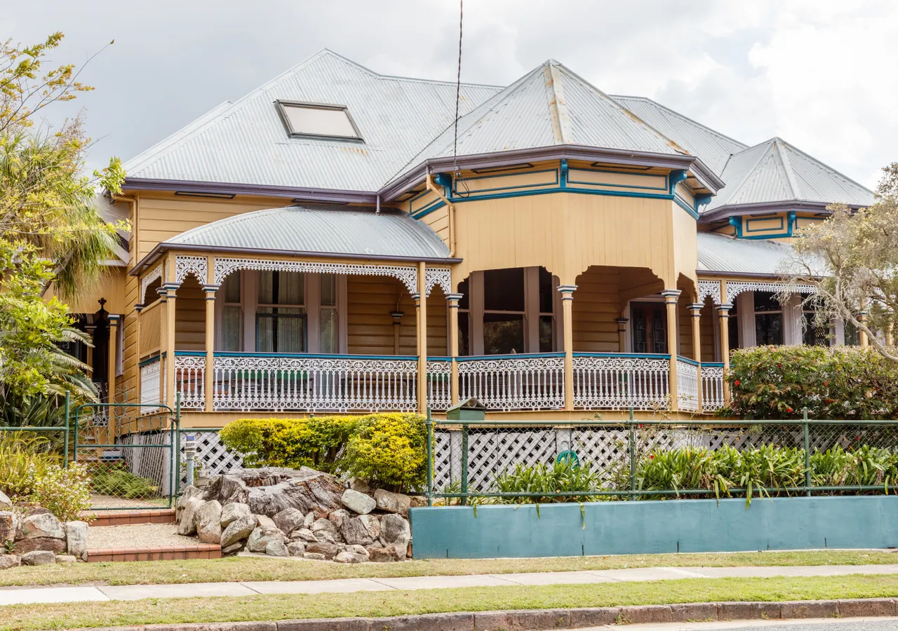A timber Queenslander home with a deep verandah, decorative fretwork and a corrugated iron roof.