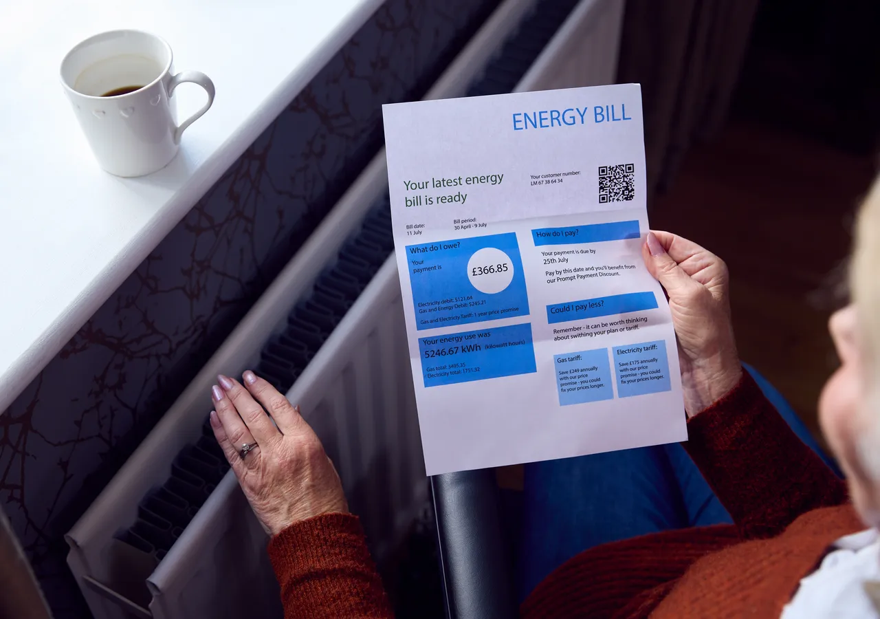 Close view of a person holding an energy bill, reading the charges summary printed on it.