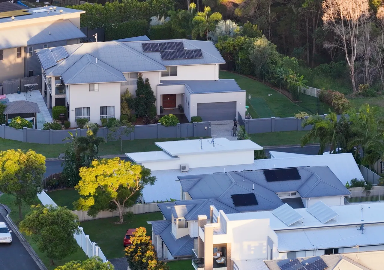 An aerial view of a suburban street of houses, several with solar panels across their roofs.