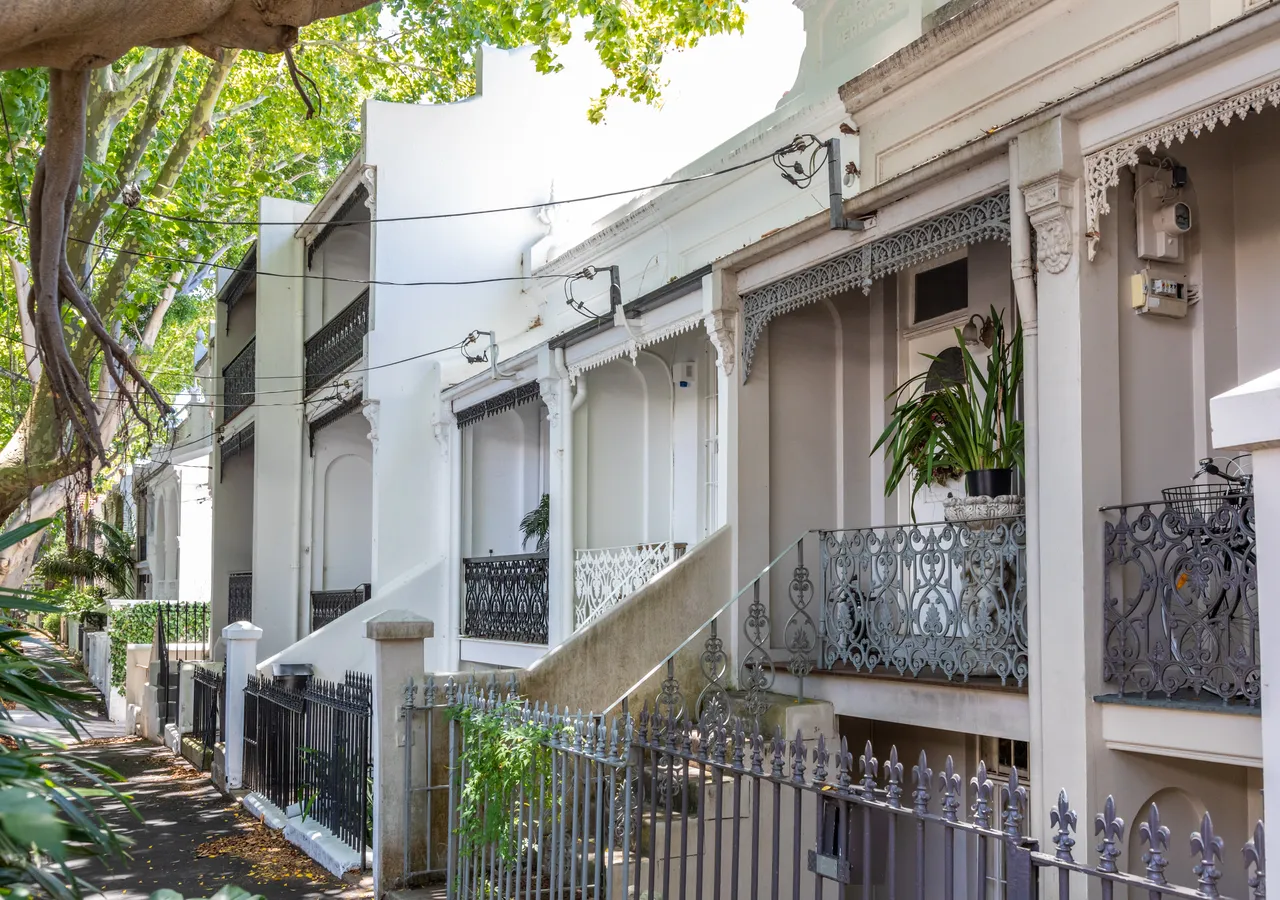 A row of inner-Sydney terrace houses with cast-iron lace balconies and small front gardens.