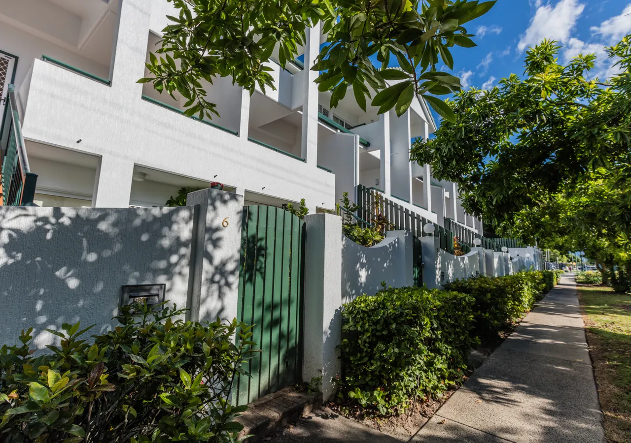 A row of white townhouses with green gates behind tropical planting.