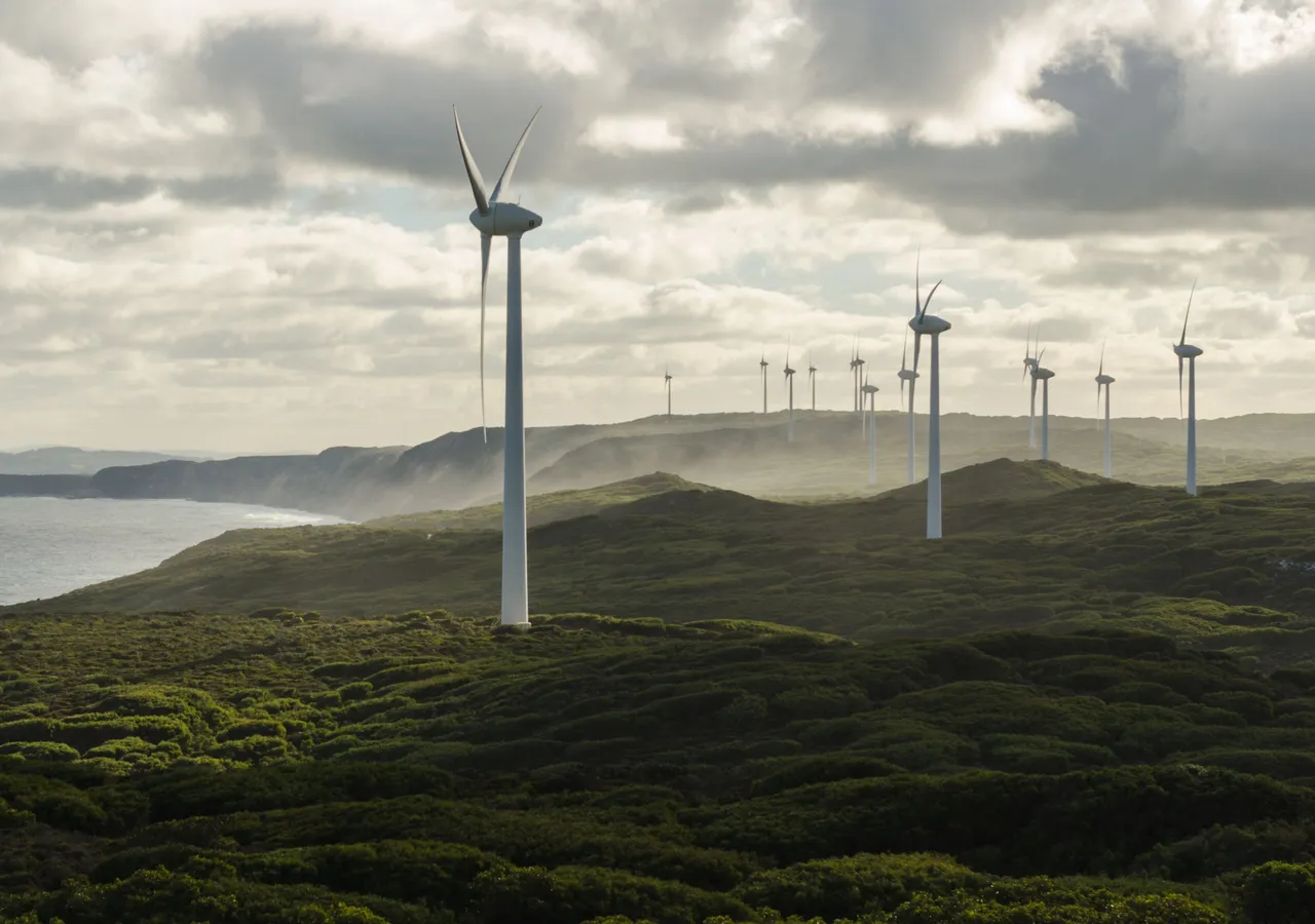 A line of wind turbines along a coastal ridge under heavy cloud.