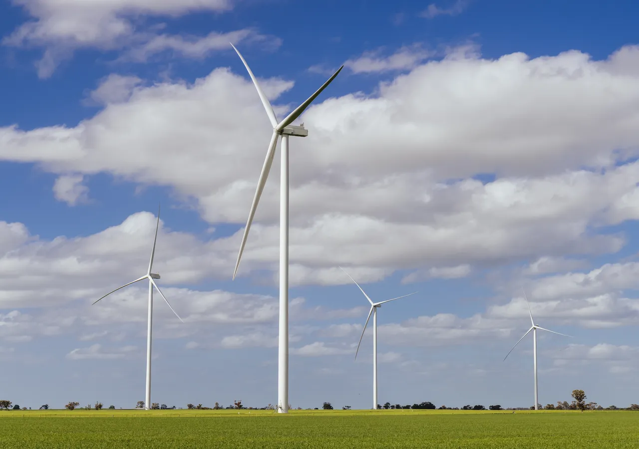 Wind turbines standing in green farmland under a cloudy sky.
