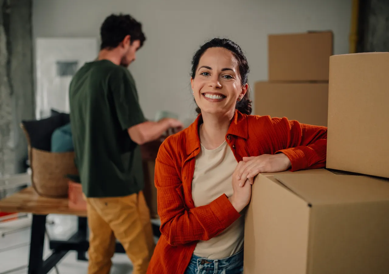 A woman smiling as she carries a cardboard box into a new home.